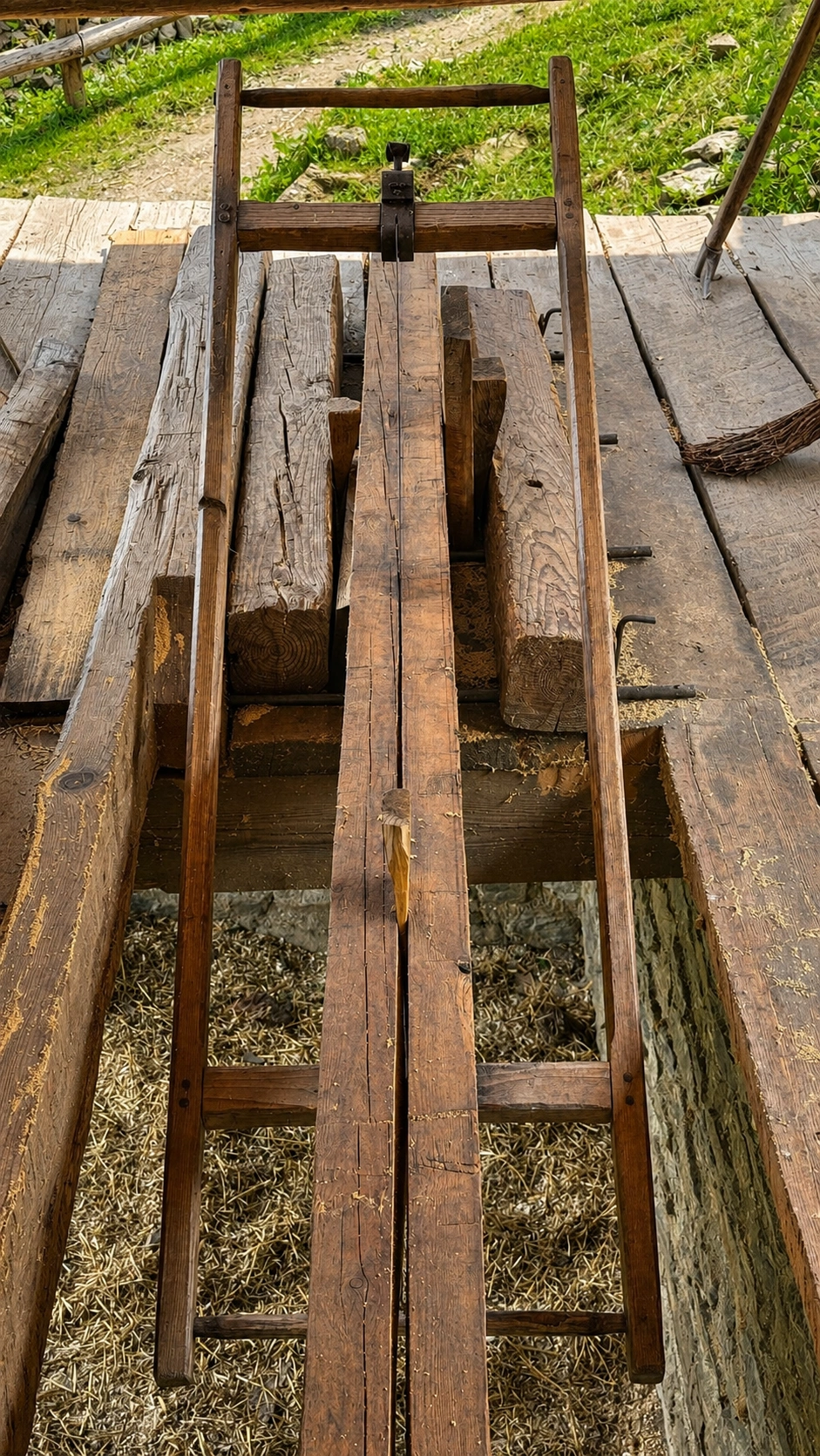 The timber is secured on a raised saw frame, allowing two workers to guide a long vertical saw through the wood.