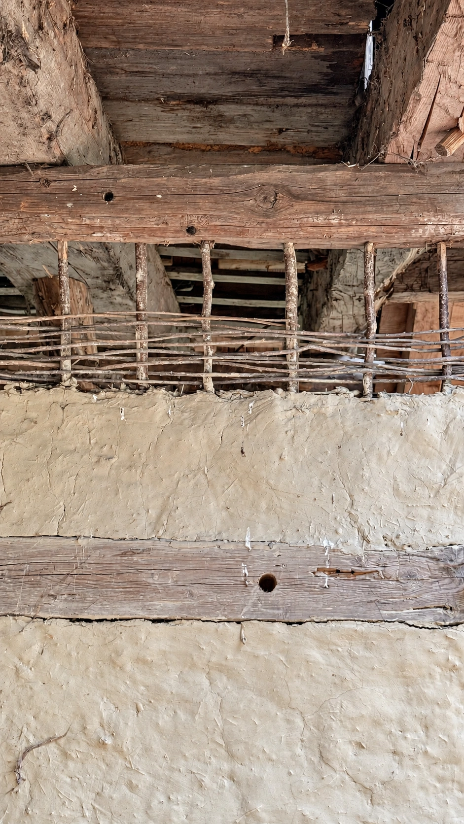 The wall shows a horizontal beam, exposed wattle framework, daubed wall and lower timber member.