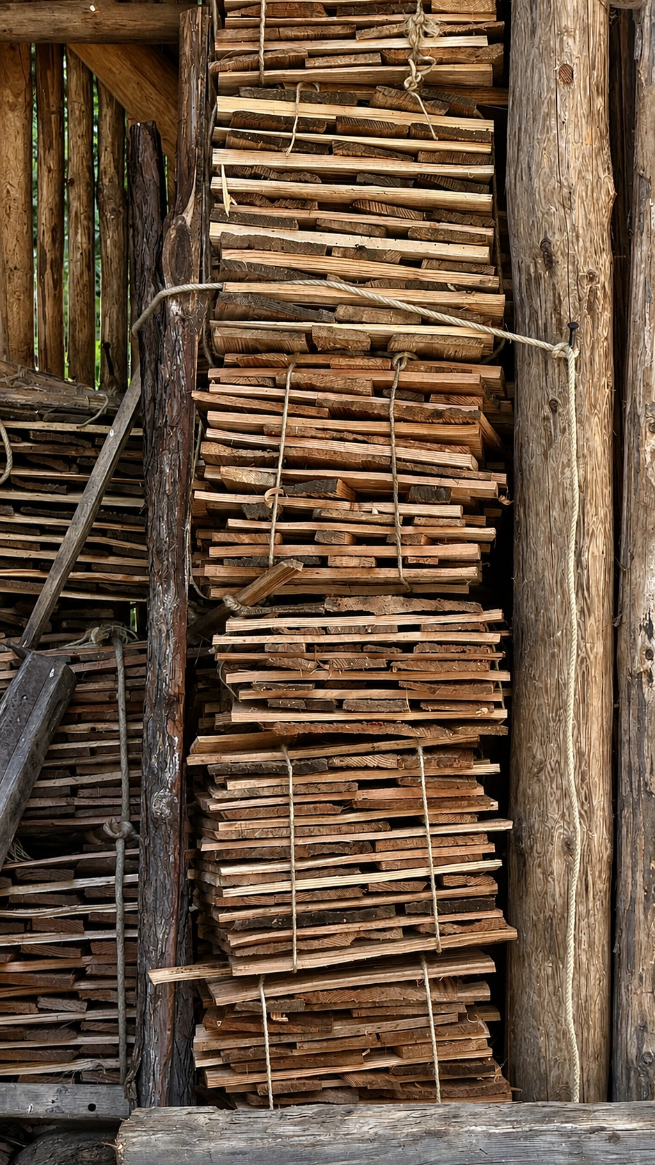 Multiple tied bundles of shingles are stacked for seasoning under cover, before use.